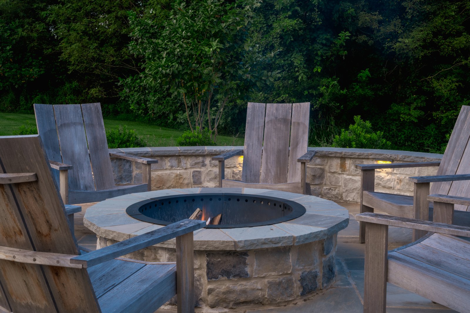 Lit stone fire pit ringed with Adirondack chairs