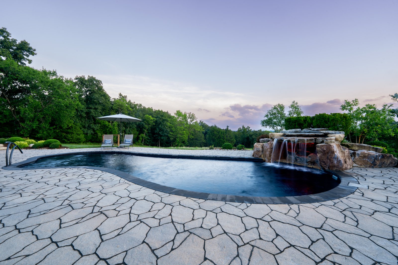 Free-form pool and flagstone terrace under a violet dusk sky